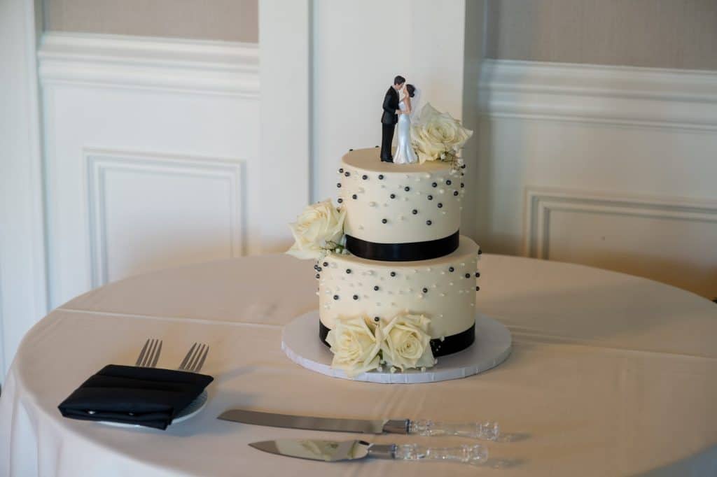 A two-tier wedding cake with black and white decorations on a table with cutlery.
