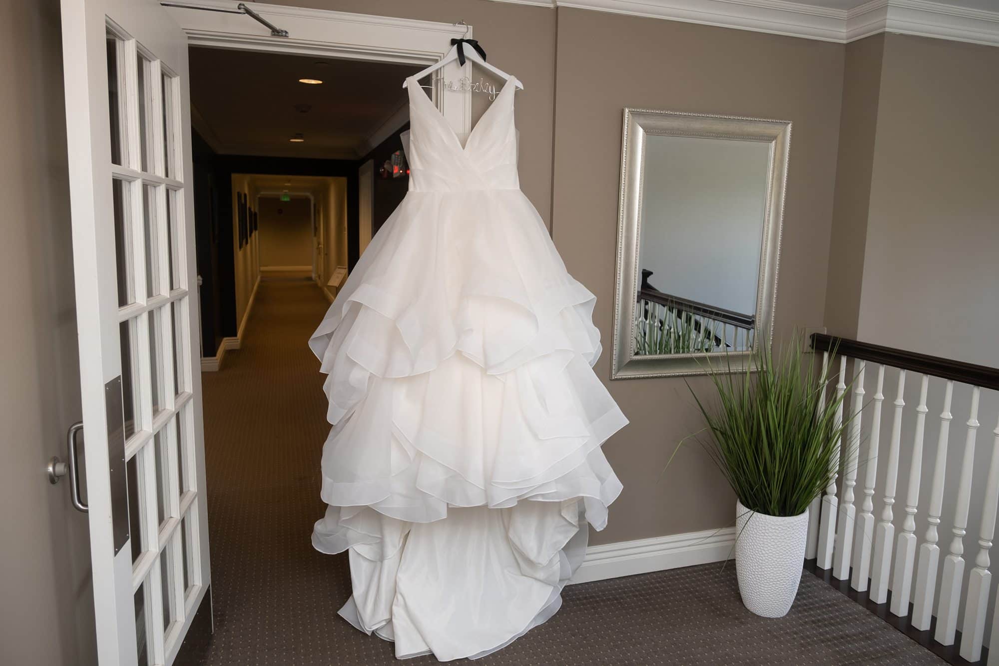 A white wedding dress with a ruffled skirt hangs on an open door.
