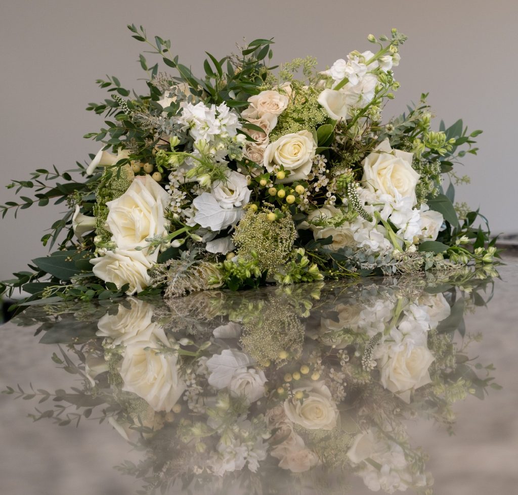 A lush floral arrangement with white roses, green berries, and foliage reflected on a surface.